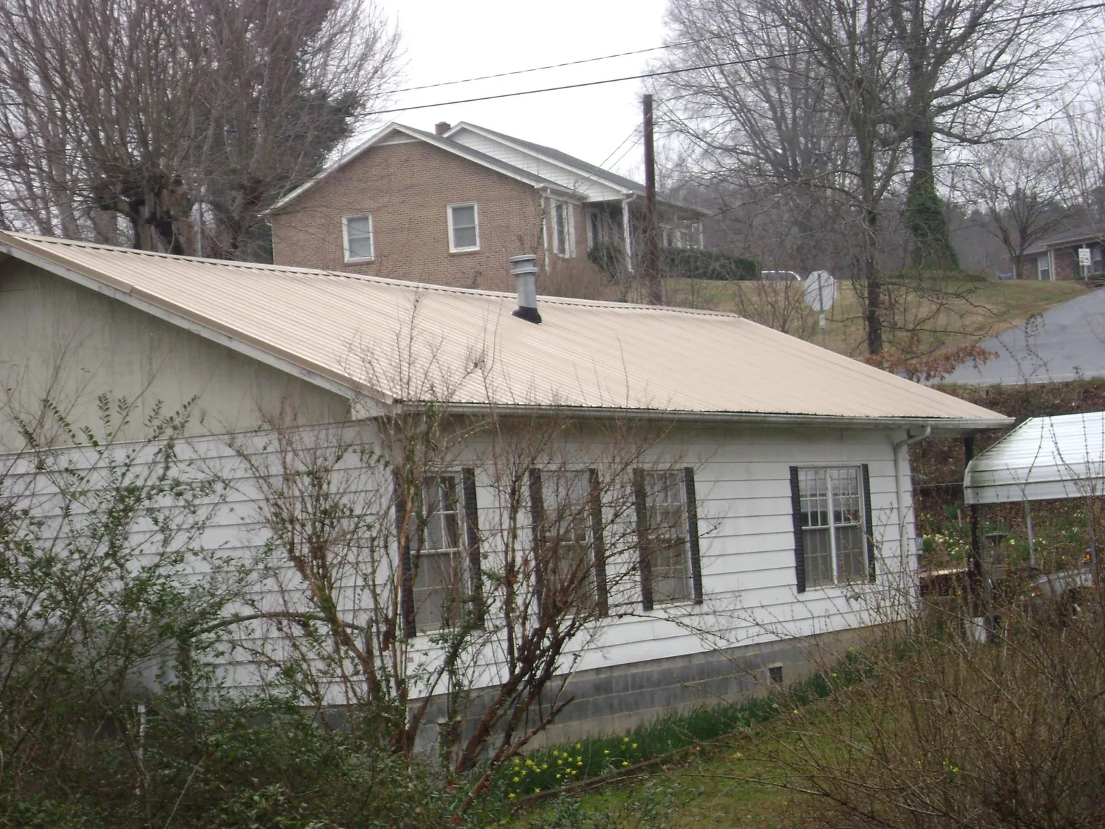 Tan metal roof on a white sided house set into a hillside — Commercial Roofing by Roofing Brothers in Jefferson